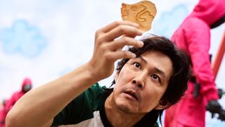 Gi-hun looking carefully at an umbrella cookie in Squid Game.