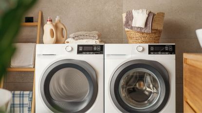 A washing machine and dryer next to one another with a laundry basket and detergent bottles on top