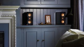 Monitor Audio Studio 89 bookshelf speakers sitting on blue shelf in lifestyle setting
