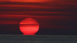 A red sun rises but appears to melt back towards the horizon
