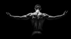 Rear view of healthy muscular young man with his arms stretched out on black background