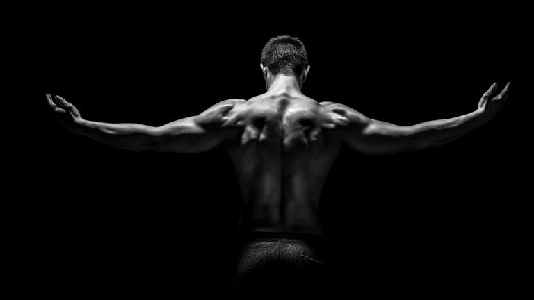 Rear view of healthy muscular young man with his arms stretched out on black background
