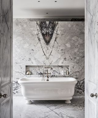 An example of small bathroom storage ideas showing a large white bath tub in a marble bathroom with storage built into the wall