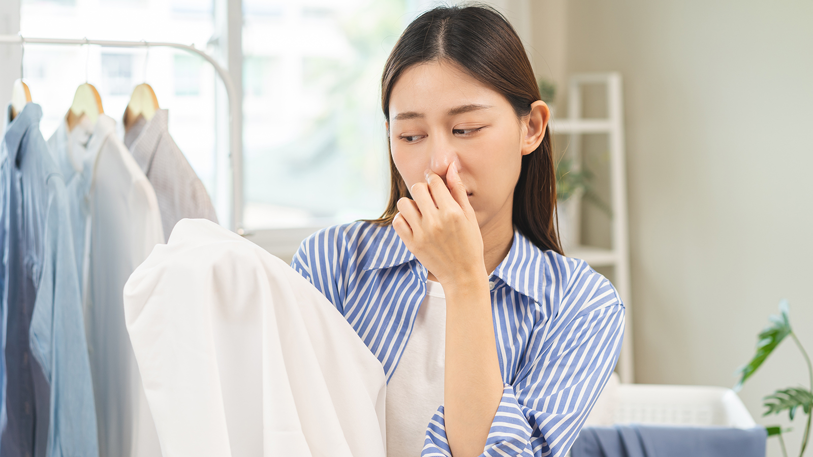 A woman holding her nose with a shirt in her hands