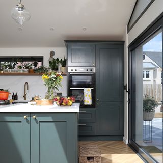 blue kitchen with tall cabinets and integrated oven and grill and kitchen island with patio doors