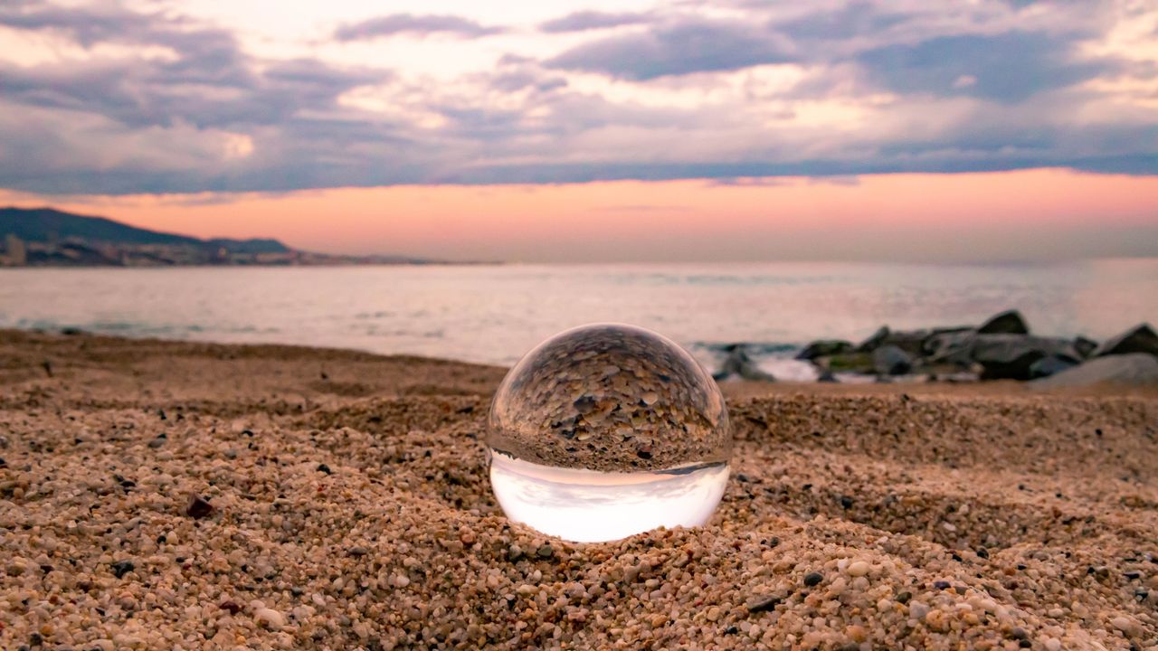 A crystal ball sits on the beach with a sunset in the background.