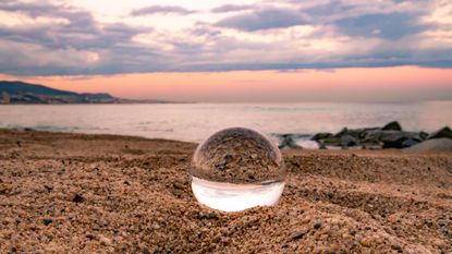 A crystal ball sits on the beach with a sunset in the background.