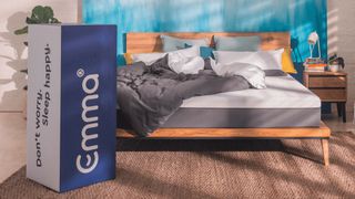 The Emma Mattress placed on a wooden bed frame positioned against a blue bedroom wall 