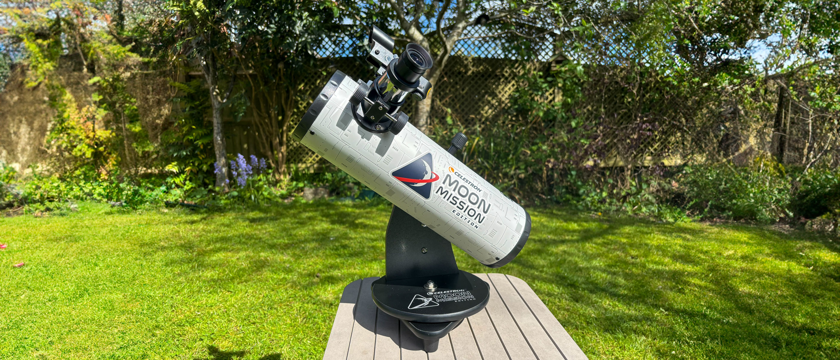 The Celestron Moon Mission 100mm Tabletop Dobsonian with grass and trees in the background.