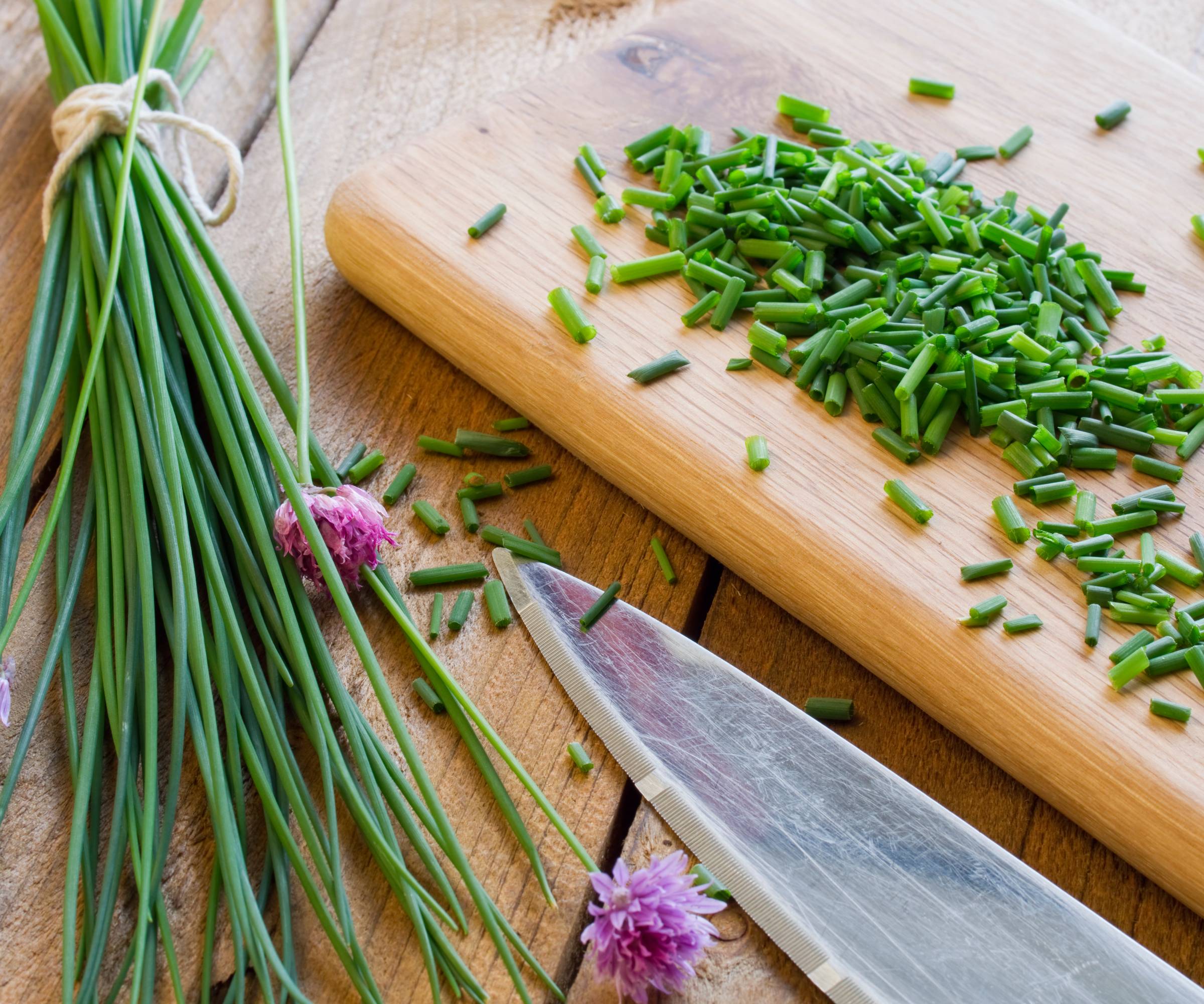 Chopped and whole chives on a cuttingboard with a knife
