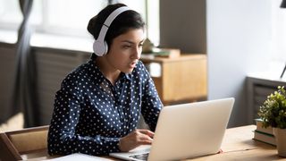 Femme portant des écouteurs et utilisant un ordinateur portable.
