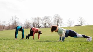 Women perform burpees in a park