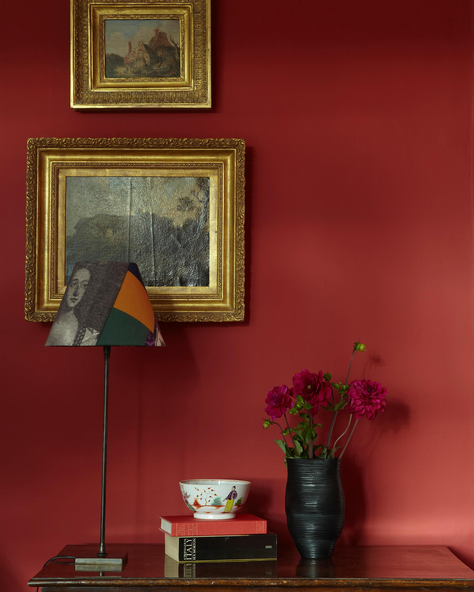 Living room painted in red with gold framed oil paintings above a console table.