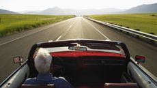 The view of an older man from behind as he drives an open convertible down an open country road.