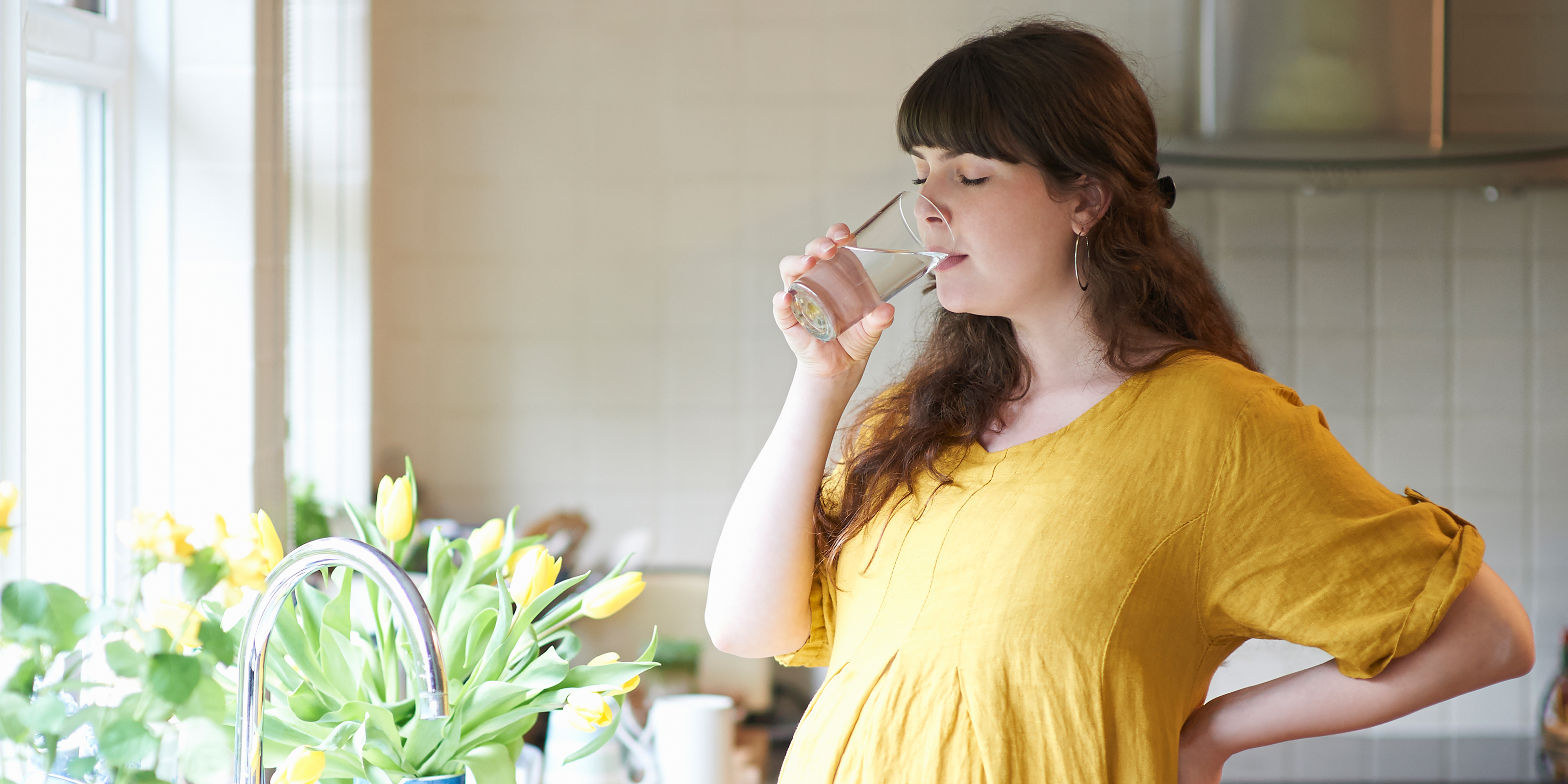 Pregnant woman drinking glass of water in kitchen at home. - stock photo