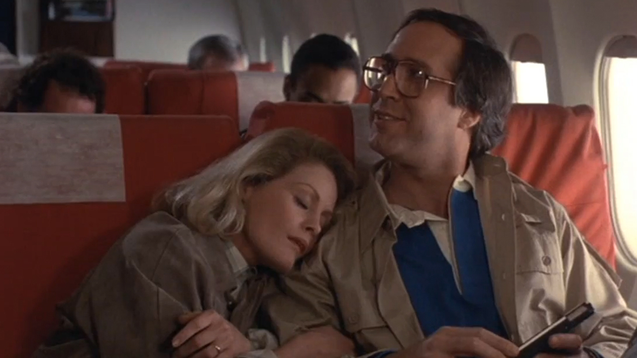 Chevy Chase smiling and looking up while sitting on a plane with Beverly D'Anglelo sleeping on his shoulder