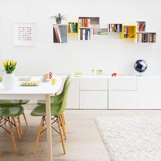 dining room with white wall and box shaped wall mounted shelves white dinning table and green chairs