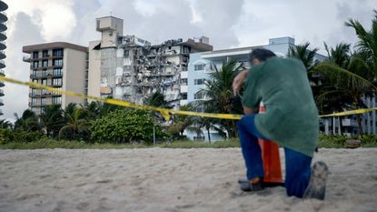 A man kneels with his head down in front of the collapsed condo building in Surfside, Florida.
