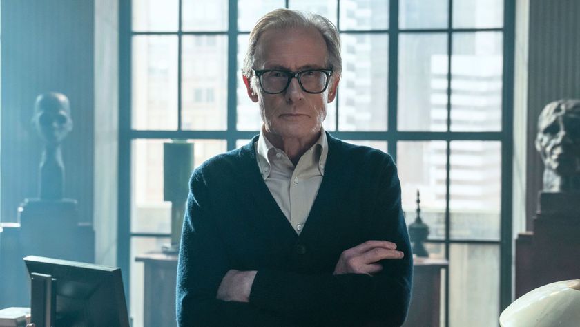 Bill Nighy stands in front of a desk with his arms folded
