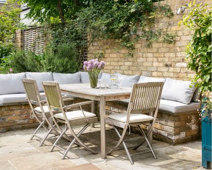 Patio costs illustrated in a walled garden with wooden table, chairs and bench seating to show the cost of laying a patio.