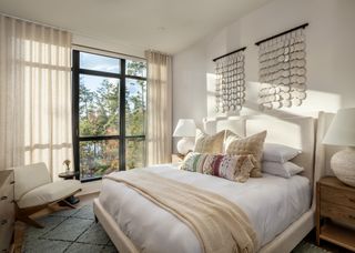 A bedroom with a cream bed, gray rug, and light flooding in through a large window