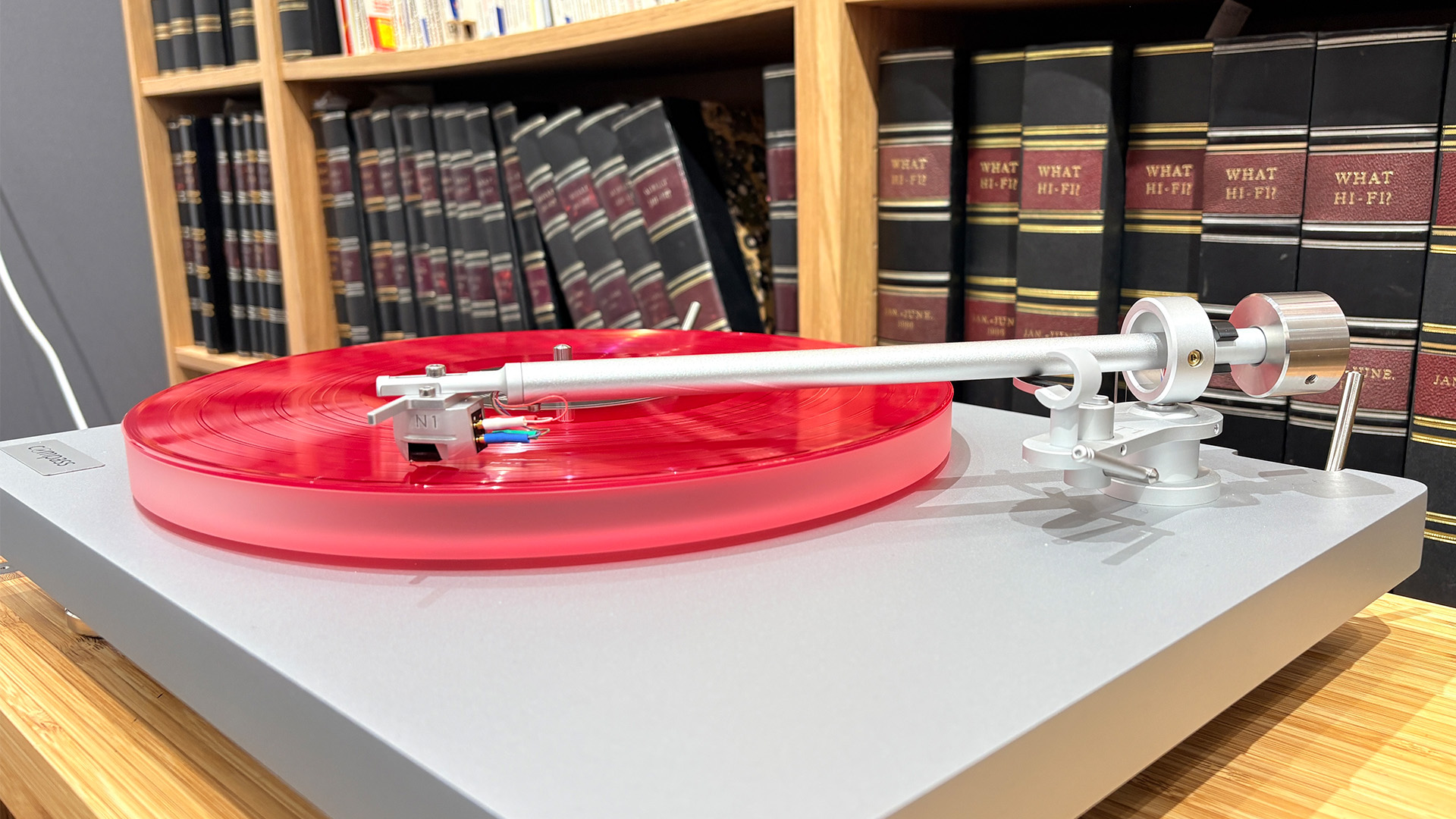 Clearaudio Compass turntable on wooden hi-fi rack with red vinyl being played, slight angle with focus on tonearm