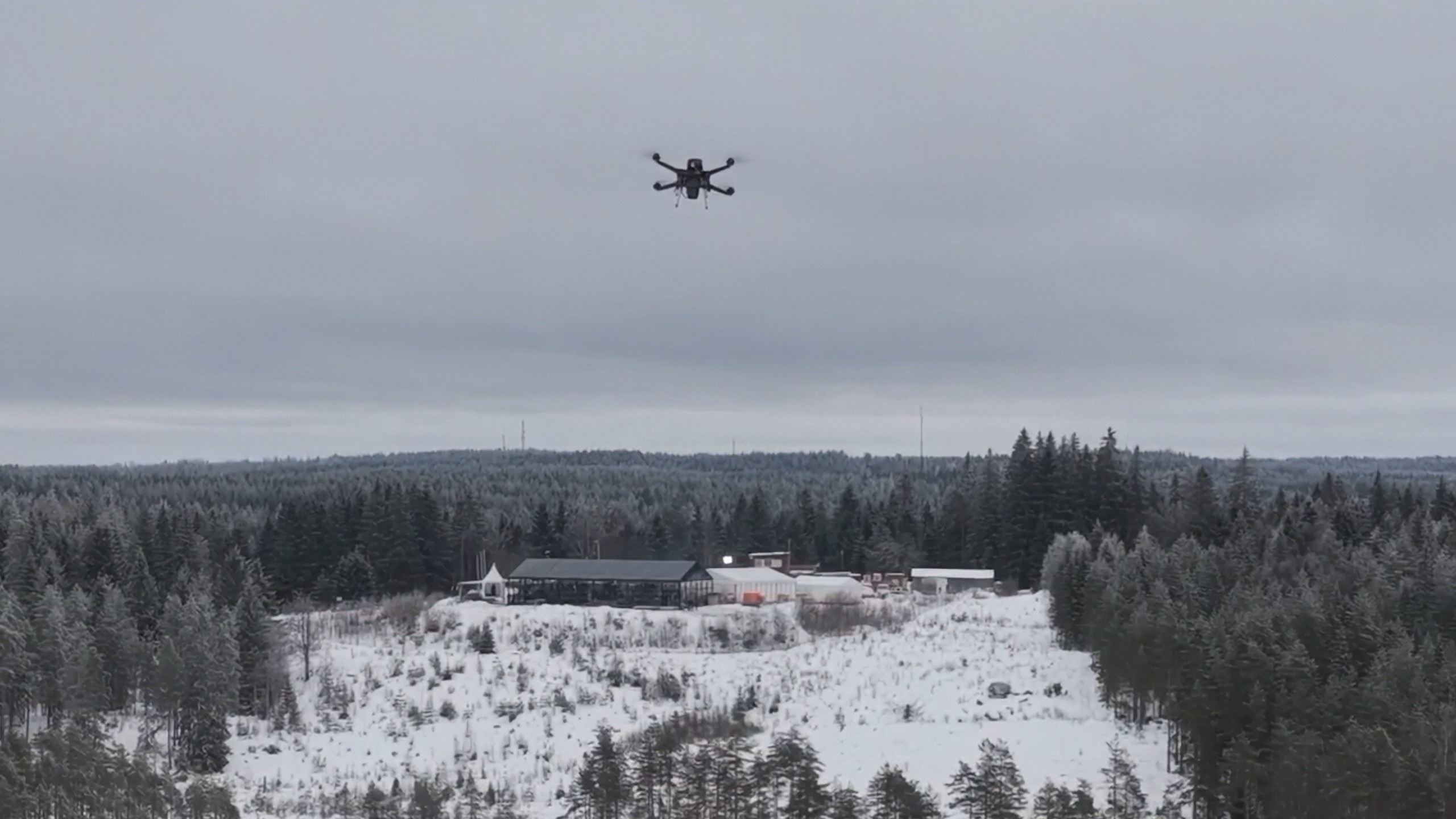 A multirotor drone flying over a snow-covered clearing.