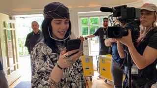 Billie Eilish looking into a phone as she's surrounded by crew in Billie Eilish: The World’s A Little Blurry