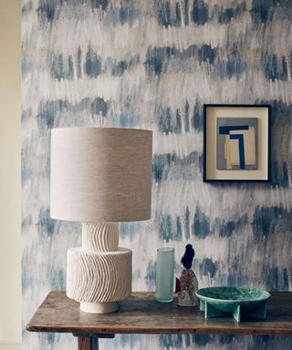 painterly sea blue wallpaper with wood console, sculptural table light and vessels