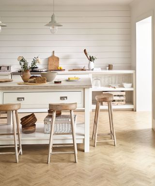 Rustic kitchen scheme with farmhouse kitchen island in neutral and wood contrast finish, wooden bar stools, and natural effect flooring