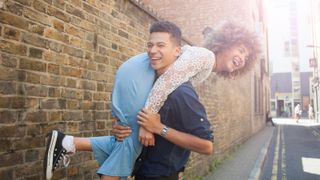 Young couple fooling around in street, man carrying woman over shoulder - stock photo