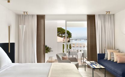 Bedroom with pale furnishings, blue sofa with pale cushions, a coffee table and sliding doors to the balcony