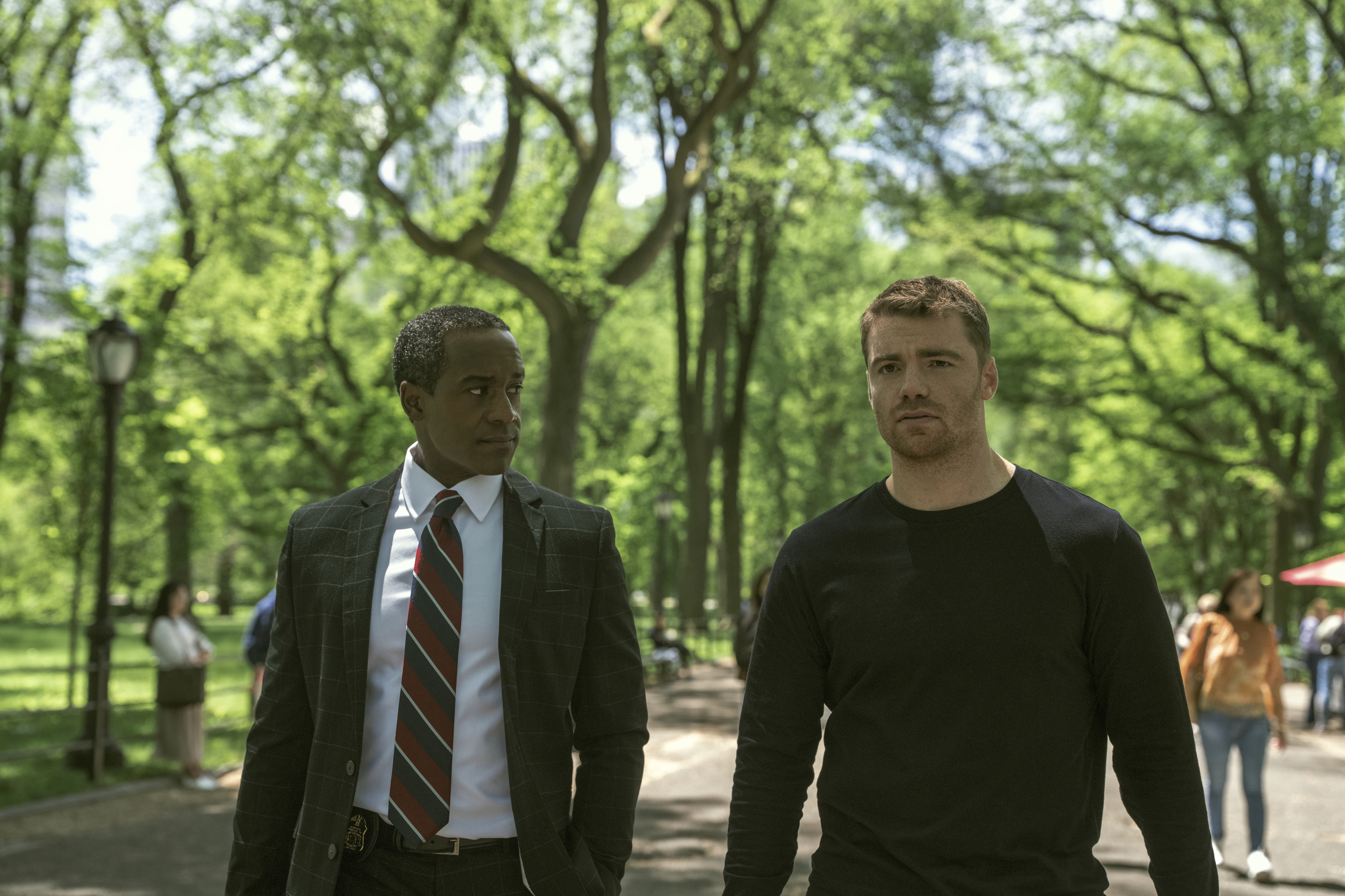Albert Jones as Deputy Director Aiden Mosley and Gabriel Basso as Peter Sutherland walking through central park while it's sunny out in a still from the night agent season 3