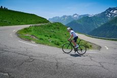 Peter Cossins ascending up a hairpin bend, snow-capped peaks in the background