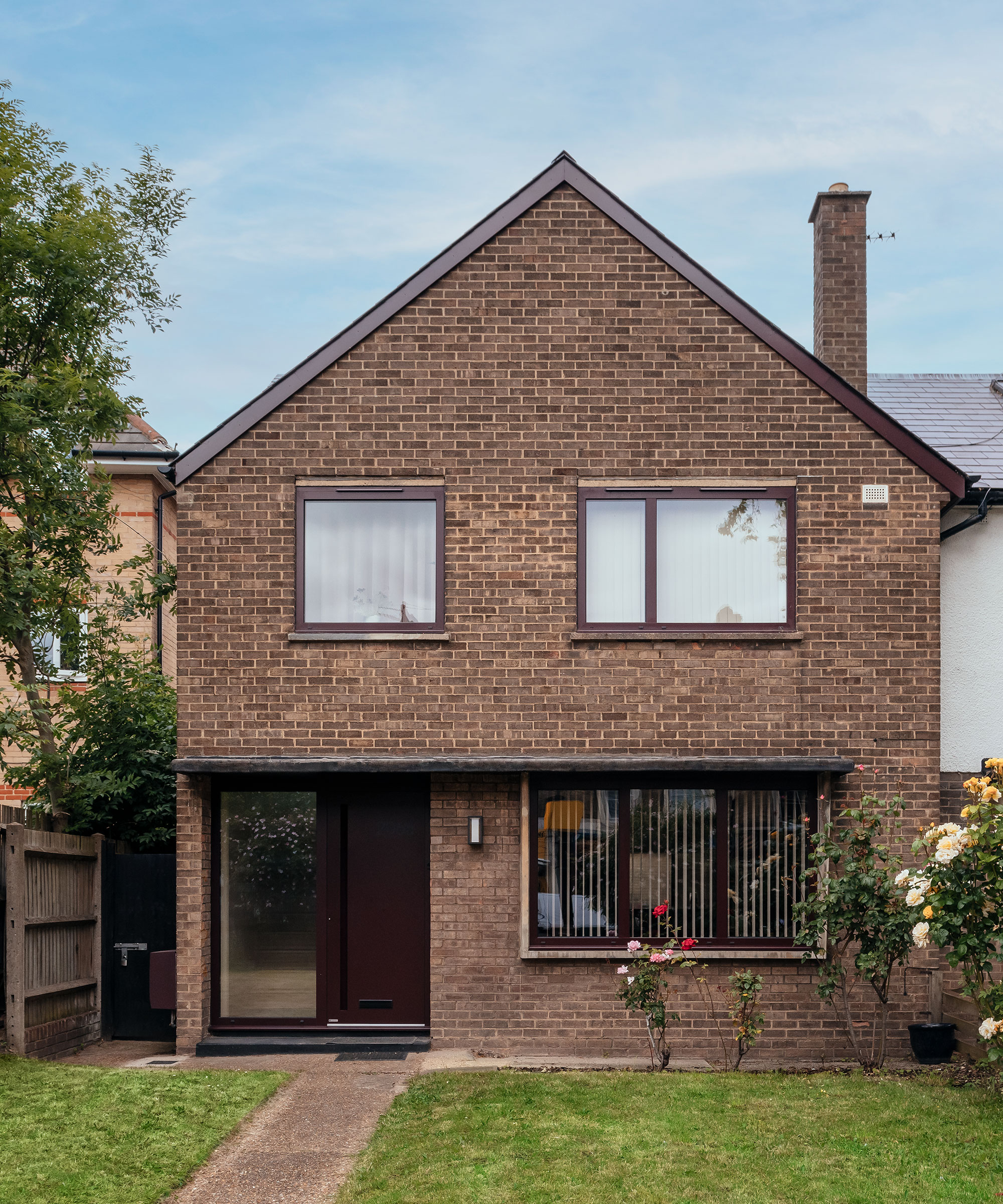 front exterior view of a brick-built terrace house with burgundy-coloured window frames