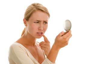 A woman looks for a cold sore in a mirror.