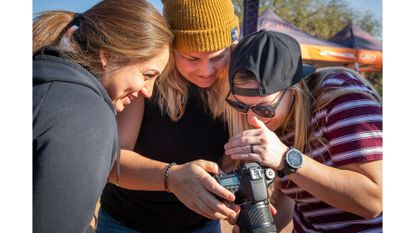 Three women at 2023 Roam Fest huddle around a camera to look at a photo recently taken. 