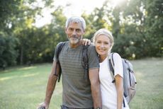 Portrait of smiling mature couple with backpacks standing in forest