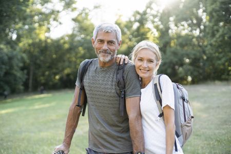 Portrait of smiling mature couple with backpacks standing in forest