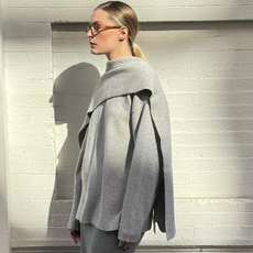 Influencer wearing gray cozy winter sweater, standing against wall.