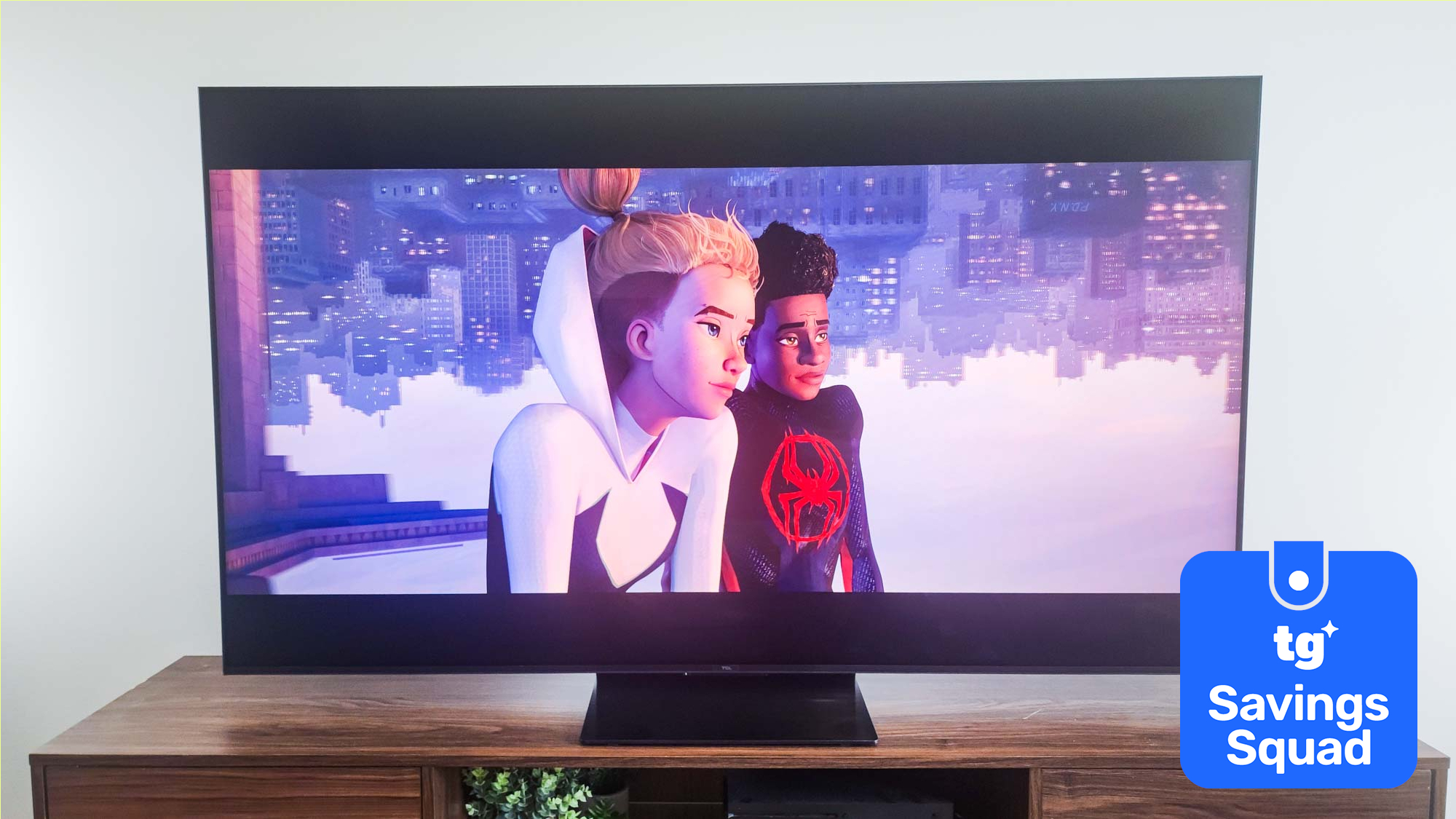 The TCL QM7K displaying a scene from "Spider-Man: Across the Spider-Verse" alongside a blue-colored badge that reads: "TG Savings Squad"