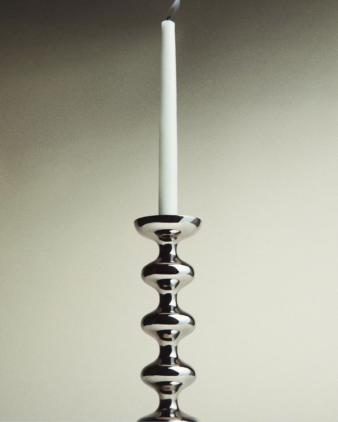 Silver Candle Holder, with a white stick candle fuming on it, against blank gray background.