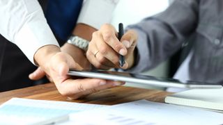 One person holds a tablet while another uses it to sign a contract