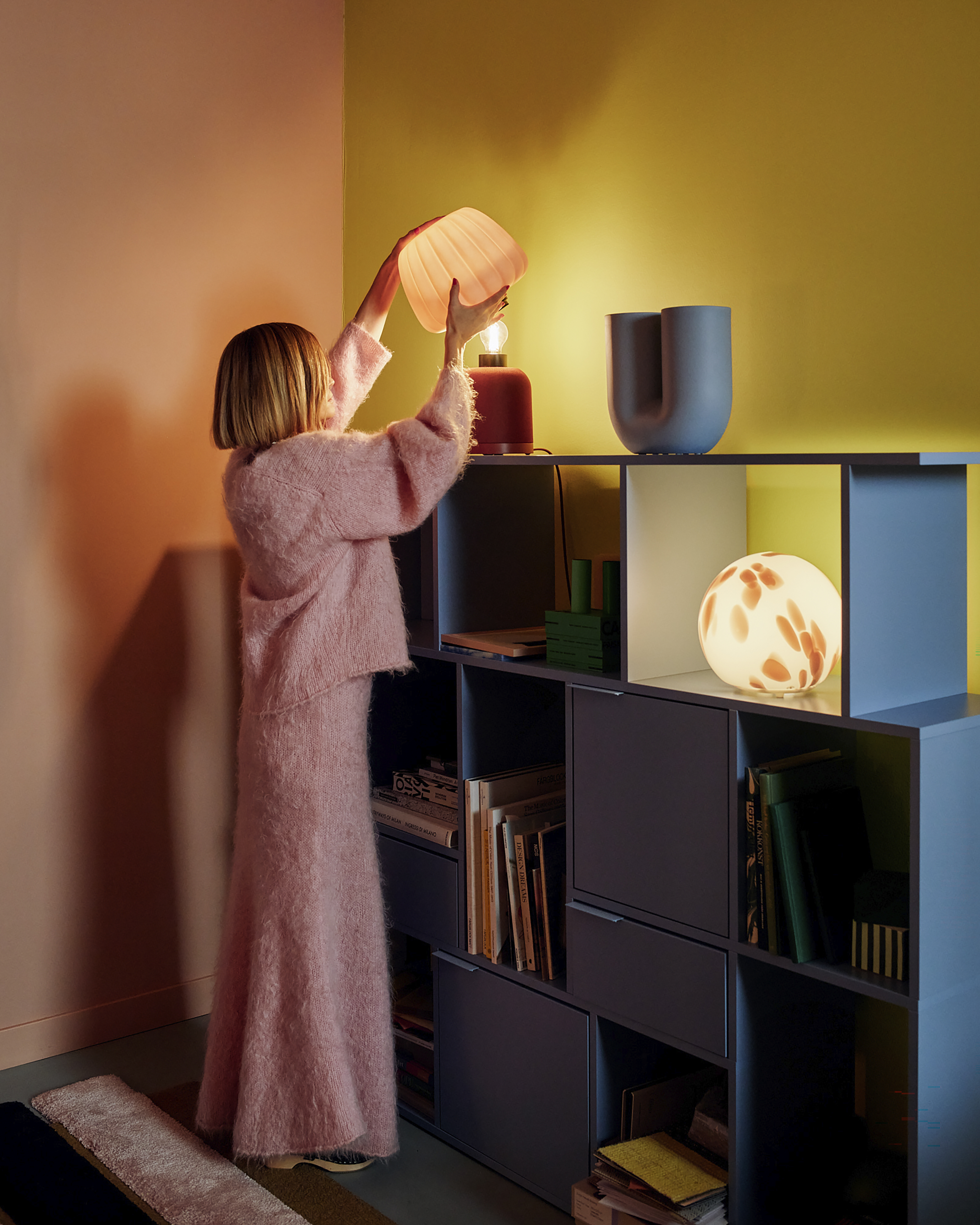 Swedish designer Teklan standing next to a shelving unit lit with lamps