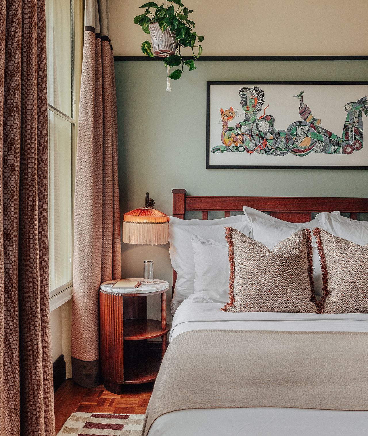 A vibrantly decorated hotel suite inspired by Bombay residences features buttery or tile blue walls adorned with original portraiture artworks, bespoke retro-fueled furnishings in wood, leather, and patterned fabric, and thriving plants.