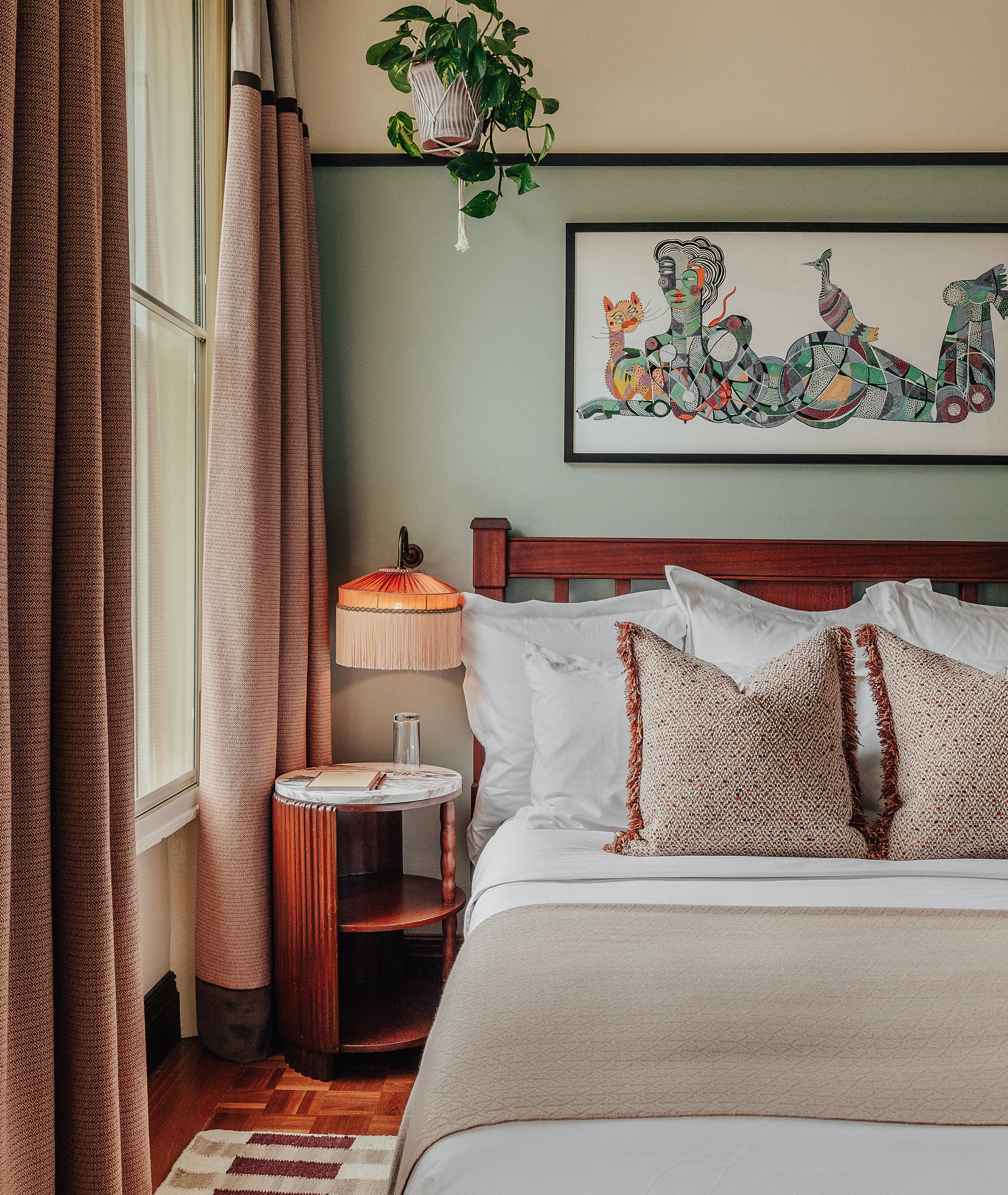 A vibrantly decorated hotel suite inspired by Bombay residences features buttery or tile blue walls adorned with original portraiture artworks, bespoke retro-fueled furnishings in wood, leather, and patterned fabric, and thriving plants.