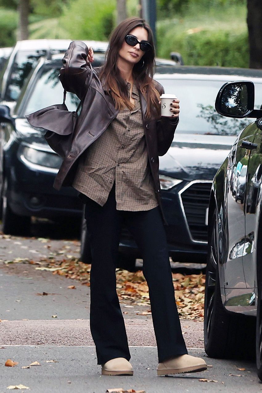 Emily Ratajkowski wearing a leather jacket, plaid shirt, black pants, and Ugg mules in London