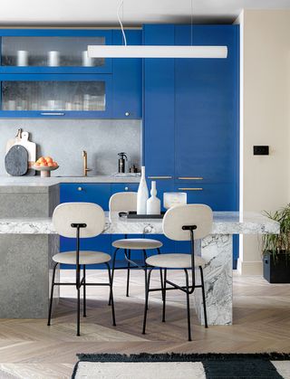 modern kitchen with blue cabinets and white chairs at a stone island