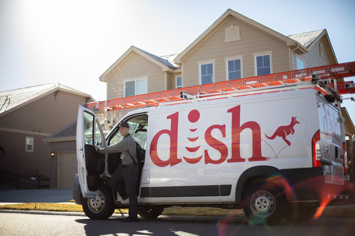 A Dish technician standing outside a company van.