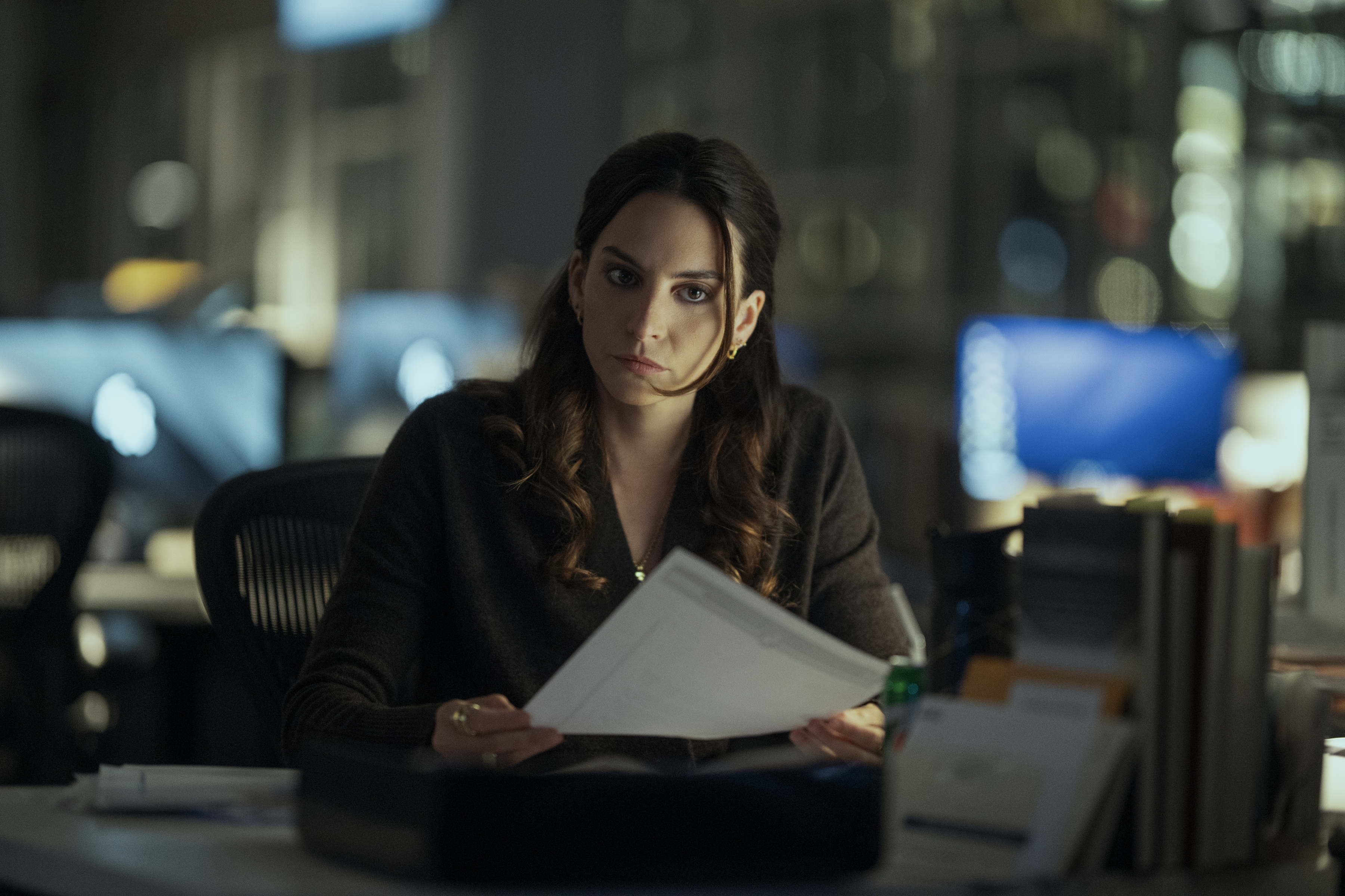 Genesis Rodriguez as Isabel in episode 302 of The Night Agent sitting at a desk in a dark office going through paper work